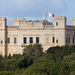 Unterwegs zwischen Misraћ Gћar il-Kbir / Clapham Junction cart ruts und Wied tal-Girgenti / Girgenti Valley - Blick aus etwa südlicher Richtung zum Verdala-Palast (Il-Palazz Verdala / Verdala Palace, Zoom). Dieser ist heutzutage die offizielle Sommerresidenz des Präsidenten von Malta. Entsprechend weht auch die maltesische Fahne auf dem Gebäude.