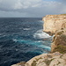 Miġra l-Ferħa - Ausblick entlang der Steilküste in etwa nördliche Richtung. Die Mündung der Schlucht von Miġra l-Ferħa befindet sich dort, wo die Klippen nach Westen (links) schwenken und im Meer der dunkle Felsen vorgelagert ist. Zwischen Fels und Klippe ist bei ruhiger See wohl auch ein natürliches Pool zu sehen, bei dem heutigen Seegang ist dies aber ständig überflutet.