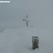 Das Gipfelkreuz taucht unvermittelt aus dem Nebel auf