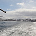 Während der Fährüberfahrt von Sørvágur nach Mykines - Rückblick nach Sørvágur. Im Hintergrund ist u. a. die Aufschüttung der Start- und Landebahn des internationalen Flughafens der Färöer zu erahnen (in Bildmitte).