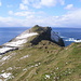 Unterwegs auf Mykines - Ganz hinten ist bereits der Leuchtturm auf Mykineshólmur zu erahnen. Links ist ein Gedenkstein zu sehen.