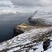 Fjallið - Ausblick aus dem nördlichen Teil des langgestreckten Gipfelbereichs. Entlang der Steilküste reicht der Blick in Richtung Gjógv. Vom Ort sind hinten im Tal einige Häuser zu erahnen.