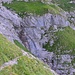 der Weg führt um den Wiesenvorsprung und durch das abschüssige Felsband (ungefährer Wegverlauf in rot angedeutet)