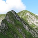 Im Vordergrund ist der heikle und etwas ausgesetzte Felskopf zu sehen, im Hintergrund befindet sich die Rinne, die auf den Gipfel führt. Die mit roten Punkten markierte Route durch die Ostflanke stösst im Sattel dazwischen hinzu.