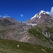 Rückblick beim Schrein საბერწე (Saberce) auf etwa 2950m auf die Vulkanlandschaft und den Gletscher გერგეტი (Gergeti) mit dem alles überragenden Fünftausender Казбек / მყინვარწვერი (Kazbek / Mqinvarcveri; 5032,8m).