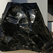 Ein Obsidian<br />Der Obsidian entsteht bei rascher Abkühlung von Lava mit einem Massenanteil an Wasser von maximal 3–4 %. Bei höheren Gehalten an flüchtigen Stoffen (neben Wasser hauptsächlich CO2) würde sich sonst, auch bei schneller Abkühlung, das Gestein zu Bimsstein aufblähen.