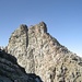 Hell beleuchtet die Ostflanke, rechts die graue Nordostflanke, über welche man zum Gipfelturm aufsteigt. Der Aufstieg zum Gipfel verläuft entweder luftig an der Kante der Ost- und Nordostflanke (Stahlseil, BH, II) oder rechts über die Nordostflanke mit BH (-4). 