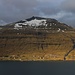 Der Reyðafelstindur (764m) und die verstreuten Häuser vom Weiler Selatrað leuchten an der Sonne über dem Meerkanal Sundini.