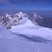 Kasbek - Ausblick von der Gipfelkuppe. Im Vordergrund sind zwei Bergesteiger zu erkennen, die gerade die steile, nicht einsehbare Gipfelflanke bewältigt haben und nun noch das allerletzte, weniger steile Stück des Aufstiegs angehen.