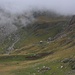 Blick von einem kleinen Plateau auf etwa 1930m auf den steileren Aufstiegsweg zur Alpebene auf 2100m-2200m. Ein Saumpfad führt die Grasflanke in der Bildmitte hoch.