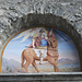 <b>Lunetta incassata nella facciata principale della chiesa di Berzona con il dipinto raffigurante San Defendente a cavallo, opera di Giovanni Meletta (1894).</b>