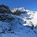 Der Steig ist nun schneebedeckt; er quert die Nordflanke der Cima Costa Brunella (links oben) hinauf zur Forcella Quarazza (verdeckt und nicht sichtbar). In Bildmitte oben die Cima Quarazza (2530 m).