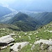 Dalla cima uno sguardo verso il fondo valle, dove si vede bene la biforcazione tra la Val Mesolcina percorsa dalla Moesa e la Riviera percorsa dal Ticino (verso sinistra). In centro foto lo spazio prativo dell’Alpe Arami con la stradina che va verso i Monti di Bedretto.