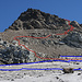 der Übergang vom Gletscher zum Geröllfeld liegt gleich neben dem felsigen Grat auf der linken Bildhälfte. die blauen Linien sind Gletscherspalten die umgangen werden, die rote Linie ist der Bergweg. Der Weg ist ohne Markierungen und im untersten Teil, im groben Geröll, sind auch keine Wegspuren zu erkennen.