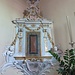 Uno dei due reliquiari posti a fianco dell'altare. In stucco0 ed ornati da teste di putti sono probabilmente opera del somazzese Carlo Moresco e sono databili al 1700 circa.