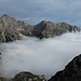 Wolken füllen das benachbarte Talbecken des Val di Larice - es zieht nach rechts Richtung Andalo hinunter.<br />Über dem Val dei Cavai ragen links die Cima San Maria (2678 m), rechts der Monte Corona (2562 m) auf.