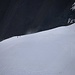 Gezoomter Tiefblick vom Verbindungsgrat zum Nordtoppen hinunter auf den Björlings glaciär. Über die Schneerampe steigen gerade zwei Bergsteiger zum Einstieg der Felswand.