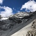 Dalla bocchetta, il sentiero appena percorso sul ghiaione sotto la Cima della Miniera. Al centro della foto, sotto lo Zebrù, baciato dal sole,  si intravede, nell'ombra delle nuvole, il tetto giallo del 5° Alpini