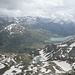 Blick nach Südosten zum Berninapass und zum Lago Bianco. Die Diavolezza-Seilbahn kommt schräg von links aus dem Tal hoch. Der Diavolezza-See in der Bildmitte trägt noch Eis, im Juli!