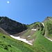 In der Mitte des Bildes befindet sich eine weitere weiss-blau-weisse Markierung (auf dem Bild schwer erkennbar). Links des kleinen Schneefelds, dort wo sich Licht und Schatten treffen, leiten einem die Markierung rechtshaltend auf den Grat.