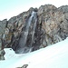 Ich komme an einem Wasserfall vorbei, während ich einen steilen Hang querend abfahre.