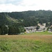 Die touristische Station Ruhestein ist erreicht. Dort gibt es Parkplätze, eine Gastwirtschaft, ein im Aufbau befindliches neues Besucherzentrum (das eckige große graue Gebäude), das bisherige kleinere Besucherzentrum (Haus mit hellroten Dach), einen Sessellift (die Talstation ist ganz rechts am Rand des Fotos) und mehrere Skisprungschanzen. Die Bushaltestelle ist derzeit wegen Straßenbauarbeiten hinten rechts an der Straße zum Schliffkopf, soll aber später wieder nach vorne zum Besucherzentrum kommen.