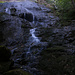 Um unteren Teil des Wasserflue Wasserfalls fliesst das Wasser über eine moosige Felsrampe und den Eingang der Bärenhöhle.