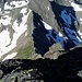 Tiefblick vom Gipfel zum Großen Horntaler Joch (Anstiegsseite). Den Grat an der Licht-Schatten-Grenze am besten in den begrünten Schrofen möglichst nahe der Hohen Villerspitze unterhalb umgehen.