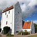 Bodilsker - An der Straße von Aakirkeby nach Nexø liegt [https://de.wikipedia.org/wiki/Bodil_Kirke Sankt Bodils Kirke], die ihre Ursprünge um 1200 hat. Der Turm steht - wie häufig in der Region - abseits (nicht im Bild). Seit Langem trägt sie den Namen der "Sankt Bodil", eine Heilige mit diesem Mädchennamen gibt es allerdings nicht: Die Kirche ist dem Heiligen Botulf, Botwulf of Thorney, gewidmet. 