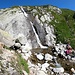 <b>Dopo il lago il sentiero si alza, supera un torrente ai piedi di una cascata e subito dopo una catena permette di rimontare in sicurezza un tratto roccioso.</b> 