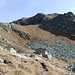 Il <b>Rifugio Gana Rossa (2270 m)</b> fa onore al suo nome: tutt’attorno ci sono “pietraie rosse”. Per onestà, occorre comunque dire che il colore è dovuto più all’erba secca che ai sassi. Più in basso un laghetto impreziosisce il paesaggio. 