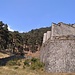 Di nuovo il particolare delle mura imponenti del Forte di Fenestrelle. La presenza al centro della foto di due escursionisti rende un'idea del rapporto delle dimensioni. Il bosco intorno al forte non era presente all'epoca, al fine di garantire la visuale delle vedette venne tagliato. La costruzione del forte iniziò nel 1728. Vittorio Amedeo II affidò l'incarico all'ingegnere militare Ignazio Bertola d'Exilles. La "prima pietra" venne posata al Forte delle Valli nella zona di Pra Catinat a 1.800 m circa di altitudine e in 122 anni di lavori si scese sino a raggiungere nel 1850 l'attuale statale che porta al Sestriere, con la costruzione della Ridotta Carlo Alberto. La ridotta Carlo Alberto è ancora visibile oggi al lato della statale non appena si raggiunge la località di Città di Fenestrelle da Torino.