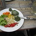 Brennesselknödel mit Salat, lecker. Anmerkung: Das kleine abgetrennte Stück des Knödels wird gleich mein Sitznachbar als Probehappen verspeisen.