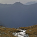 Querung eines der glitzernden Bachläufe auf der oberen Alpe della Costa, darüber schwebend Madom da Sgióf und Cima di Nimi, und rechts dahinter der Monte Limidario