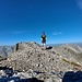 Gipfel mit Bergsteiger. Gipfelbuch kann er trotz aufwändiger Suchanstrengung keines finden.