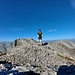 Der Gipfel mit Bergsteiger. Gipfelbuch kann er trotz aufwändiger Suchanstrengung keines finden.