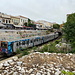 Unterwegs in Athen - Zwischen Agora und der gut besuchten Straße Adrianou juckelt die Metro oberirdisch durch das Gelände. Wie die meisten griechischen Bahnfahrzeuge trägt auch diese Garnitur viel Graffiti.
