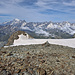 Blick vom Gipfel zum einfach über Schutt und Firn erreichbaren W-Gipfel. Dahinter über dem Grand Golliat mit seinen gut sichtbaren, noch mit Firn gefüllten NE-Couloirs u.a. Grandes Jorasses und Mont Blanc, rechts davon u.a. Aiguille de Triolet, Aiguille Verte, Aiguille d'Argentière und Aiguilles Dorées