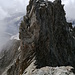 Blick vom NNE-Gipfel zum Hauptgipfel. Man klettert erst direkt an der Kante. Etwa nach einem Drittel muss man nach links hinaus und irgendwie an den kleinen, sonnenbeschienenen, vorstehenden Block kommen (leicht überhängend, IV). Darüber wird es wieder einfacher.