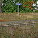 Stationsschild nach (2008) neuer Norm (früher waren sie weiss). Der starke Bewuchs zwischen den Gleisen verrät, dass hier schon länger keine Züge mehr verkehren.