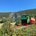 Llanberis - Nach der Rückkehr vom Snowdon erkunden wir noch kurz die Umgebung. Hier fährt ein Zug der Llanberis Lake Railway in Richtung der Endstation. Hinten ist der ehemalige Steinbruch Vivian Quarry zu sehen. Daneben sind Gebäude des National Slate Museum zu erahnen.