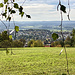 ... die Westnase des Rehbergs herunter, nochmal kurz auf Asphalt. Dort dieser  Blick zum Stadtteil "Siedlung" (darin das Haus, in dem ich großteils aufwuchs) und in der Ferne zu den Höhenzügen des Frankenjuras. Oberhalb der Bildmitte die Baumkronen des [https://www.hikr.org/gallery/photo3999775.html?post_id=190384 legendären Kroahwäldlas.]