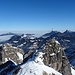 Das Gipfelkreuz des Ponten steht auf dem (niedrigeren) österreichischen Gipfel, dahinter die Tannheimer Berge und das Alpenvorland unter einer dichten Nebeldecke.