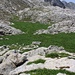 Die auffällige Alpebene Alpebene Katun Grlata auf etwa 1800m mit zwei verfallenen Alphütten. Der Bergweg quert die grüne, flache Bergwiese. Auf der anderen Seite leitet dann der markierte Bergweg durch Karstgelände hinauf ins Hochtal Skripa.