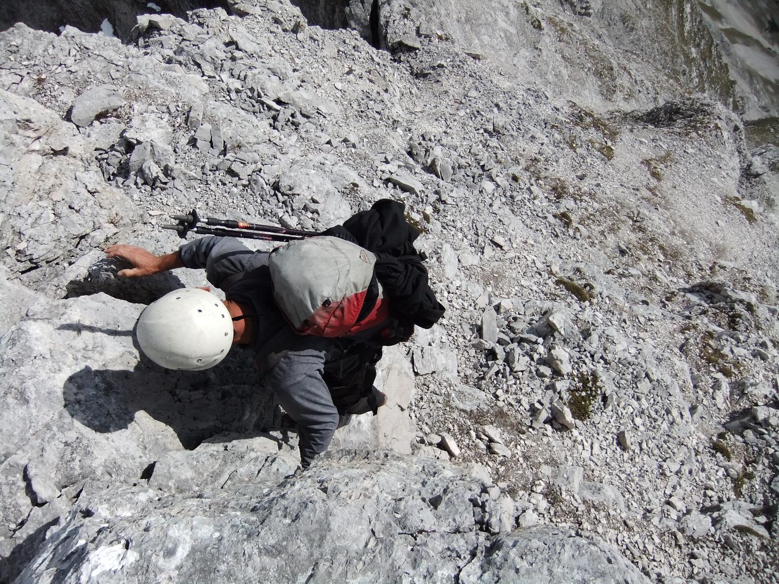 Frau in einem gelben Rüstungs-Outfit sitzt auf einem Felsvorsprung in der Nähe des Gipfels eines Berges, während sie ins Tal schaut.