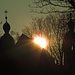 Die untergehende Sonne hinter der Silhouette der Hl.- Kreuz- Kirche mit den zwei Rokoko Hauben-Türmen in Landsberg