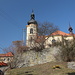 In Třebušín - Blick vom Marktplatz zur Kirche. Links ist ein Stück des (gelb markierten) Weges auf den Berg Kalich zu sehen.
