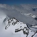 Monte Leone (3553,4m): Gipfelaussicht auf den Alpjergletscher links des Gratkammes mit P.3424m mit dem sturmumtobten und wolkenverhangenen Breithornpass (3347m) dahinter. Rechts des Gratkammes sind Spalten auf dem Chaltwassergletscher zu sehen.