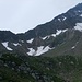 Über diese Schutthalde und der Traverse oberhalb des Felsbandes (oberhalb der tiefsten Schneefelder) führt ein Band auf den Grat etwas südlich von Punkt 2374. Oberhalb eines Schneefeldes ist der grosse weisse Pfeil, der den Einstieg markiert, sichtbar.