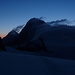 Eiger und Mönch. Auf dem Jungfraujoch sind Lichter zu erkennen. Wolkenschwaden ziehen über das Joch und die Gipfel.